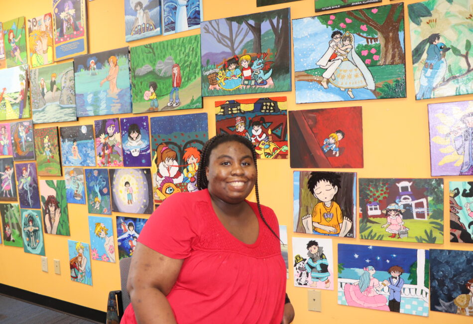 Elizabeth, an artist from Fine Line Studios, is standing in front of her artwork.