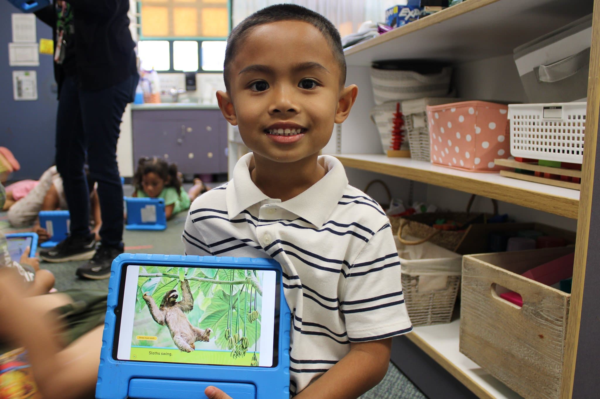 Smiling student holding a tablet with a book about a sloth on the screen.